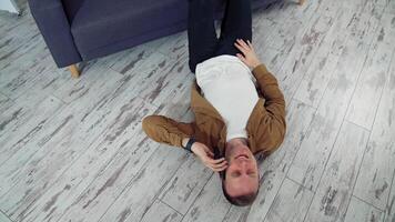 Young man talking the phone at home. Happy man having a conversation through the phone while lying on floor near the sofa. Top view. Quarantine. video