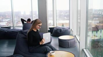 Business woman with a notebook sits in office. Female office worker has some problems with a laptop and shaking it. Faulty device in woman's hands. video