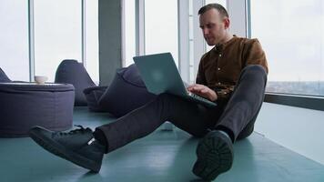 Young man sitting on floor near the window with a laptop. Happy man winning something while using a wireless computer. video