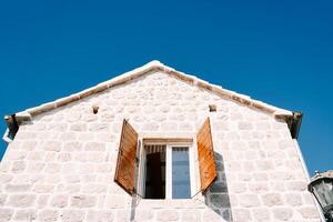 Open wide wooden shutters of the attic window of an ancient stone house photo
