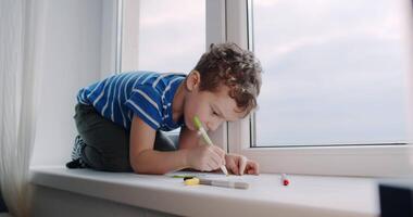 A boy finds peace on a window sill, expressing creativity through art video