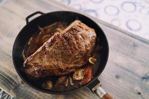 Roast beef with vegetables stands in a pan on a wooden table. Top view photo