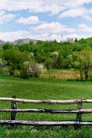 Wooden fence on a green field with mountains in the background photo
