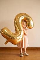 Little girl stands in a room with an inflatable number two in her hands photo