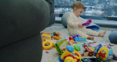 A small baby is happily sitting on the floor, engaged in playing with toys video
