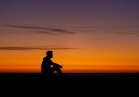 Man Sitting in Silhouette Enjoying a Colorful Dramatic Sunset photo
