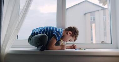 A boy on a window sill joyfully explores creativity using art supplies video