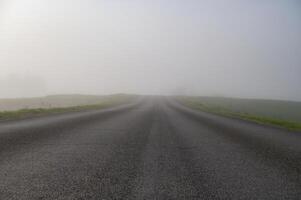 Misty road stretches into the distance, disappearing into a thick layer of atmospheric fog. photo
