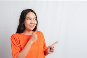 A woman smiling and pointing to the side with both hands by wearing orange tshirt photo