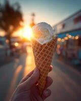 A person holding an ice cream cone with the sun setting in the background photo
