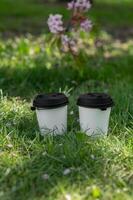 Two coffee cups on the grass with a tree in the background photo