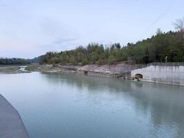 Serene riverside with forest background and concrete structure at dusk photo