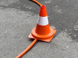 Orange traffic cone on wet asphalt with cable passing through base photo