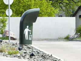 Unique modern trash can on street corner with icon for litter disposal and greenery in background photo