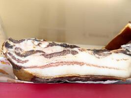 Thick slices of raw bacon on red surface displaying marbled fat layers photo
