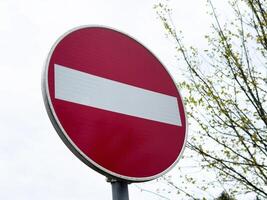 Red do not enter sign against cloudy sky and leafless tree in background photo