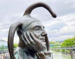 Bronze jester sculpture with amused expression against cloudy sky photo