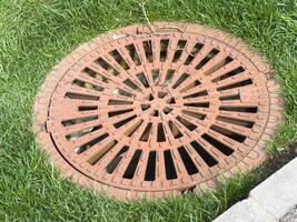 Round metal manhole cover on grass with circular pattern and letters photo