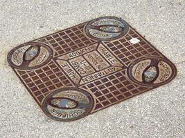Rectangular metal manhole cover on concrete surface with brand names photo