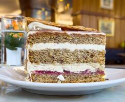 Delicious layered walnut cake with cream and raspberry jam on white plate photo