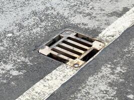 Rusty roadside drain on weathered asphalt with white line photo