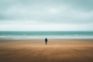 A lone person standing on a beach in front of the ocean photo