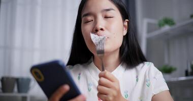 Handheld low angle view shot, Beautiful Asian woman enjoys eating fruit while playing with mobile phone happily at home. Relax at home, Enjoy healthy food video