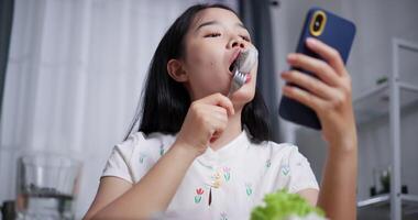 Handheld low angle view shot, Beautiful Asian woman enjoys eating fruit while happily calling with friends on mobile phone at home. Relax at home, Enjoy healthy food video