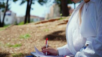 Collage showcasing a young woman meticulously writing in her notebook while sitting on the ground in a park, surrounded by trees and dappled sunlight video
