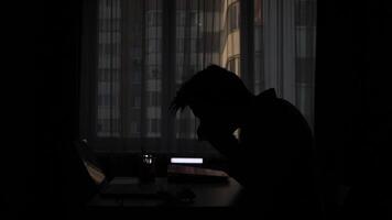 silhouette of a sneezing man in the office at his desk with a laptop video