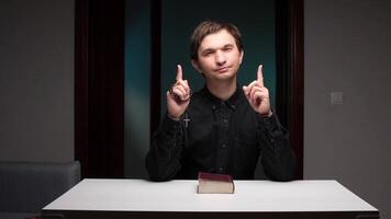 Preacher pointing upwards while sitting at table with holy book video