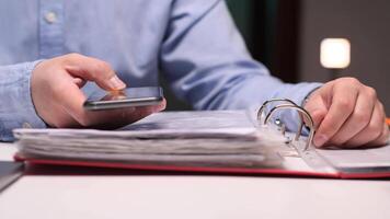 Businessman using smartphone and consulting documents in binder video