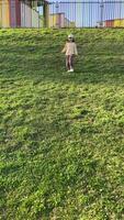 vertical little Girl running on grass near colorful fence, enjoying childhood and freedom video