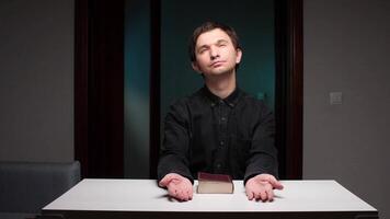 Religious man praying with open hands and holy book on table video