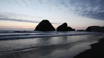 Ocean Waves Flowing On Sandy Beach With Large Silhouetted Rocks In Background video