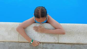 Young girl wearing goggles, lounging at the edge of a swimming pool, enjoying the clear blue water during a sunny summer vacation filled with relaxation and fun video