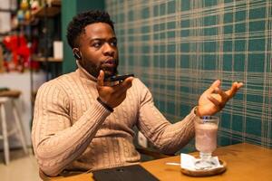 Distraught African American man holding his mobile phone and discussing something with worried look while sitting in coffee shop. photo