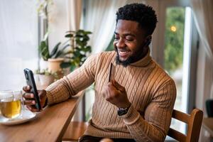 Stylish young African man with credit card in hand, ready to make an online purchase while sitting at cafe, using his smartphone for an effortless e commerce experience. photo