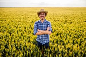 Portrait of successful farmer with arms crossed standing in a wheat field and enjoying the success of his cultivated land. photo