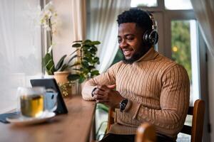 Happy and confident African American man using headphones and digital tablet to work remotely while sitting at table in cafe. photo
