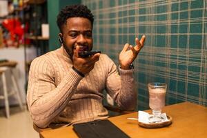 Distraught black man on an call via phone, visibly displeased, indoor cafe setting with hot beverage and smartphone, realistic emotion and expression. photo