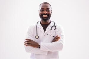 Portrait of successful African doctor who is smiling with arms crossed while standing proudly on gray background. photo