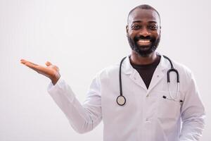 Portrait of smiling African American doctor who is holding blank space for your advert on gray background. photo