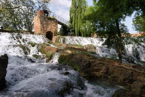 Beautiful cascading waterfall in a serene natural setting surrounded by lush greenery and historical ruins photo