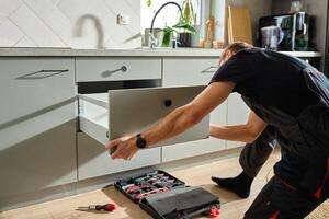 Handyman installing and adjusting drawer slide mechanism in contemporary kitchen. Furniture installation photo