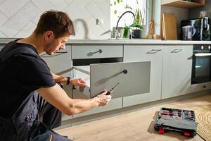 Man assembling kitchen drawer in modern cabinet using screwdriver photo