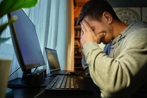 Exhausted man at home office with hands on face after long work hours photo