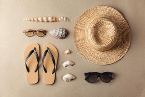Flat lay of beach items including straw hat, sandals, sunglasses and shells on sand background photo