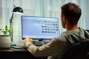Back view of man working from home at desk with computer and lamp photo