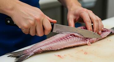 Chef expertly filleting a fish, showcasing precision and culinary skill. The glistening fish fillet, knife, and cutting board create a visually appealing scene. photo